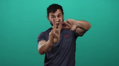 Sakallı İspanyol bir adam canlı yeşil bir arka plana karşı bir hashtag sembolü yerleştiriyor, rahat bir gömlek giyiyor, neşeli ve dostane bir ifade yayıyor..