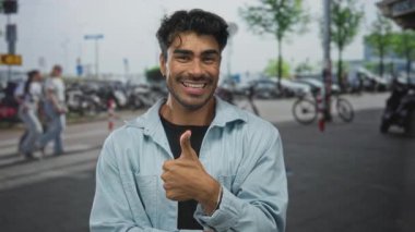 Sokakta park halindeki bisikletlerin arasında elleri kulaklarına dolanmış ve ifade vermek isteyen Latin asıllı genç bir adam..