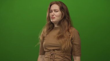Yüzü yeşil stüdyo arka planında elleri olan beyaz bir kadın, omuzlarından dökülen saçlar ve çilli deri; iğrenme..