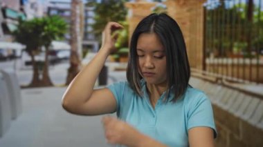 Mavi gömlekli genç Asyalı kadın şehir manzarası ve palmiye ağaçlarıyla çevrili şehir sokaklarında hayal kırıklığına uğramış görünüyor. Sıkıntı ve tefekkür duygularını aktarıyor..