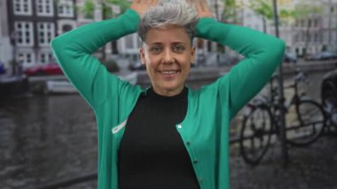 Kadın, yeşil hırka ve şehir sokaklarında rahat bir ifadeyle siyah gömlek giyerek el ele tutuşuyor..