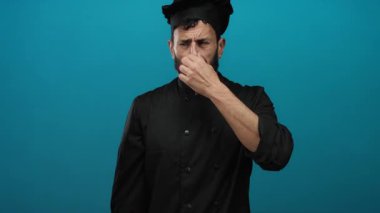 Siyah üniformalı İspanyol aşçı burnu kötü kokuya tepki veriyor. Mutfak ortamındaki iğrenme ifadelerini vurguluyor..