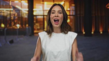 İspanyol bir kadın şehir sokaklarında parlak bir gülümsemeyle bulanık bir şehir zeminine karşı şaşkınlığını dile getiriyor. Enerji dolu canlı bir açık hava anını yakalıyor..