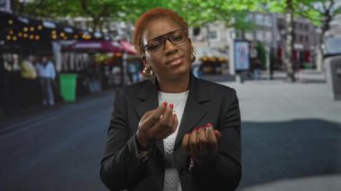 Siyah ceketli ve beyaz gömlekli bir kadın para içinde avuç içi kaldırıyor. Meşgul şehir caddesinde jest yapıyor. Çaresizlik..