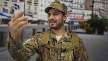 Askeri üniformalı adam, apartmanlarla dolu kalabalık bir şehir sokağında telefon görüşmesi yapmak için akıllı telefon tutuyor; bağlantı iletişim yoldaşlığı servisi.