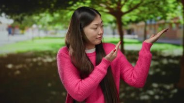 Pembe kazaklı kadın ağaçların altındaki parkta şaşkın şaşkın bakıyor güneş ışığı yaprakların arasından süzülüyor..