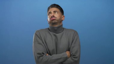 Gri balıkçı yaka kazaklı, kolları çapraz ve elleri çenesinde genç İspanyol adam stüdyoda tefekkür.