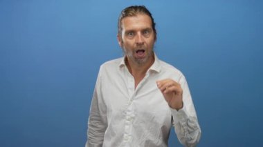 Uzun sarı saçlı ve beyaz gömlekli bir adam el ele tutuşup mavi stüdyoyu dinliyor..