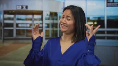 Şehir sokaklarında el kol hareketi yapan mavi gömlekli kadın gündüz vakti şehir ortamında açık havada neşeli bir ifade sergiliyor..