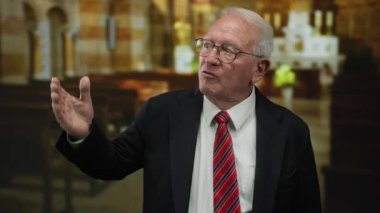 Takım elbiseli kıdemli bir adam kilise ortamında tutkulu bir şekilde jest yapar, dini mimari ve kilise kiliselerinin resmi geçmişiyle duygularını ifade eder..