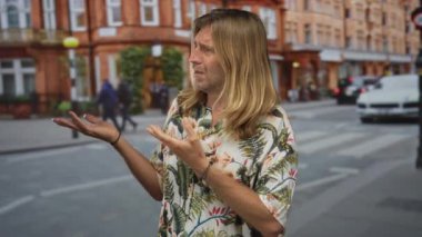 Uzun saçlı, parlak çiçekli gömlek giyen sarışın bir adam işlek bir şehir caddesinde avuçlarını açık gösteriyor..