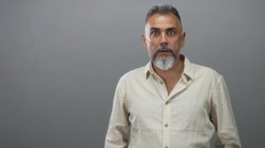 Gri stüdyoda her iki işaret parmağı açık bir ağızla kamerayı işaret eden adam, sürpriz dikkat nişanı.