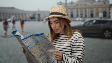 Şapka takan genç bir kadın, arka plandaki ikonik mimariyi gösteren St. Peter Meydanı, Vatikan 'daki bir açık hava ortamında harita okuyor..