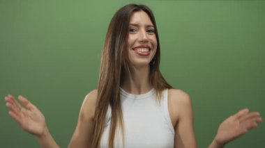 Beyaz kolsuz bluz giyen gülümseyen genç İspanyol kadın iki elini yeşil bir stüdyo duvarına kaldırıyor..