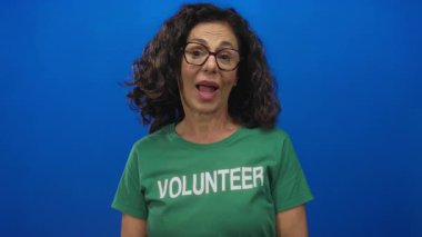 Orta yaşlı İspanyol kadın yeşil tişörtlü gönüllü stüdyoda dil uzatıyor; küstahlık eğlenceli mutluluk sevinci.