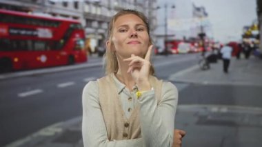 Londra 'nın arka fonunu işaret eden samimi bir kadın portresi. Sokakta kendine güvenen ve sıradan görünen kırmızı bir otobüsün yanında sarışın bir adam var..