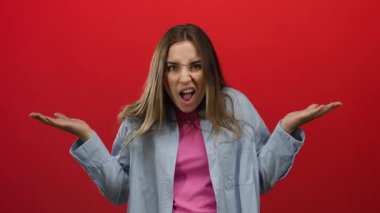 Kırmızı arkaplan karşısında şaşırdığını ifade eden bir kadın. Pembe gömlekli, mavi ceketli, genç görünümünü vurgulayan sarı saçlı sıradan bir tarz sergiliyor..