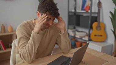 Dostum, şakaklar ağrıyor, dizüstü bilgisayara bakarken onları okşuyor İspanyol genç erkek evde oturup sinirli ve stresli hissediyor..