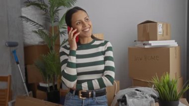 İspanyol kadın telefonda konuşurken gülümsüyor. Etrafı kapalı evdeki bitkilerle dolu kutularla çevrili..