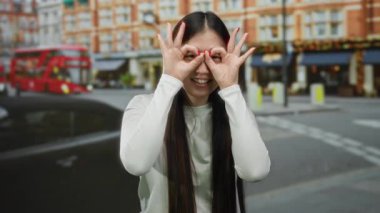 Arka planda ikonik kırmızı otobüslerle gülümseyen kadın şehir ortamında neşeli bir ifade ve neşe sergiliyor.