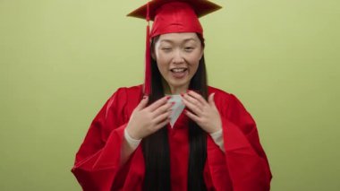 Kırmızı kep ve cübbeyle mezuniyeti kutlayan kadın, izole edilmiş sarı bir arka plana gülümsüyor, heyecan ve neşe ifade ediyor..