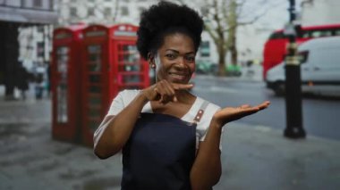 Önlüklü kadın şehir sokaklarında ikonik kırmızı telefon kulübeleriyle Palm 'ı işaret ediyor..