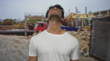 Güneş ışığı altındaki şantiyede yumruklarını sıkarken başını geriye doğru eğen genç adam, kollarını kaldırdı..