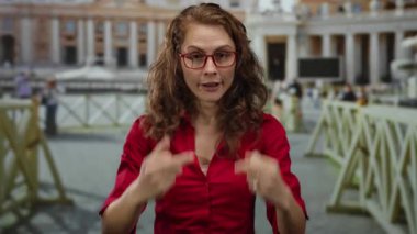 Kırmızı gömlekli kadın Aziz Peter Meydanı 'ndaki Vatikan' da el hareketi yapıyor. Bulanık insanlar ve arka planda mimari anlayışı açık havada tutumunu gösteriyor..