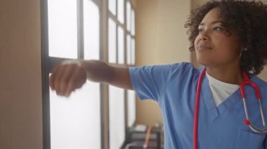 Steteskoplu kadın doktor kafasını büyük bir binanın penceresine yaslıyor; yorgunluk stresi.