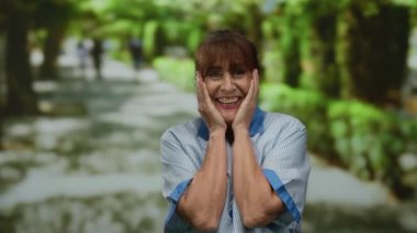 İspanyol kıdemli temizlikçi kadın açık hava parkı ortamında mutlu bir şekilde gülümsüyor yeşil bir arka plana karşı neşeli bir ifade sergiliyor..