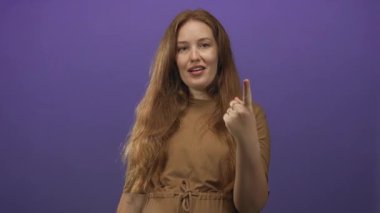 Genç kadın gülümsüyor ve mor stüdyoda iki parmağını kaldırarak barış ve zafer işareti yapıyor..