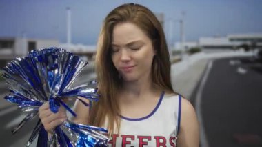 Genç beyaz kadın açık havada parlak mavi ponponu tutuyor. Trafiğe somurtuyor..