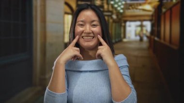 Canlı bir şehir caddesinde gülümseyen genç bir kadın dükkanların ve ışıkların bulanık arka planıyla.