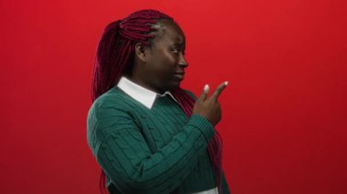 Yeşil süveterli, pembe örgülü kadın kırmızı arka plana yan bakan düşünceli görünüyor..