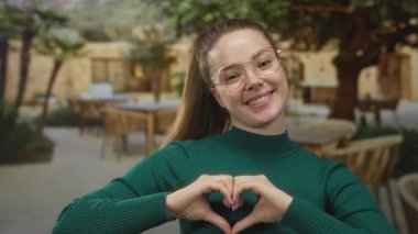 Gülümseyen kadın, elleri açık bir restoranın terasında kalp hareketi yapar..