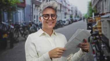 Park halindeki bisikletlerle dolu bir kaldırım taşı caddesinde çarşafları tutarken katlanmış kağıt belgeleri okuyan kadın, merak odaklanıyor.