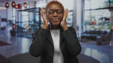 Otel lobisinde elleri olan bir kadın gözlük, ceket ve kolye takıyor. Kendine güveniyor..