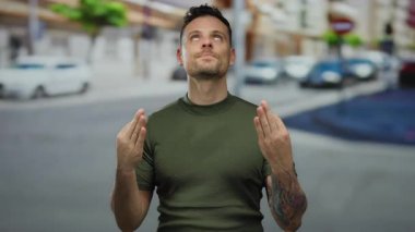 Dövmeli genç adam şehir sokağında dikiliyor. Açık gökyüzü altında arabalarla ve binalarla çevrili gündelik kıyafetlerle düşünceli görünüyor.