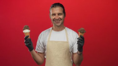 Parlak kırmızı bir stüdyoda eldivenli iki dondurma külahını tutan önlüklü bir adam. Mutlu bir seçim..