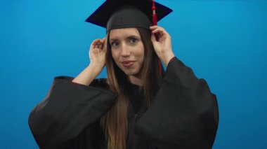 Mezuniyet elbisesi giymiş genç İspanyol kadın havan topu püskülünü elleriyle stüdyoda ayarlıyor; başarı gururu.