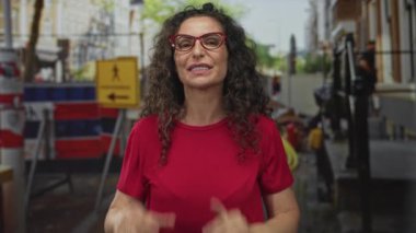 İnşaat alanında gözlüklü bir kadın, elleri ağızlarına dolanmış, haykırıyor, kendine güveniyor..