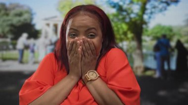 Ormandaki parlak yeşil ağaçların arasında gülerken ve gülümserken her iki avucunu yanaklarına bastıran kadın; neşe.