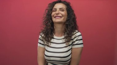 Kadın başını eğiyor ve gülümsüyor, çizgili bluz giyiyor, çıplak kollarıyla ve kıvırcık saçlarıyla stüdyoda..