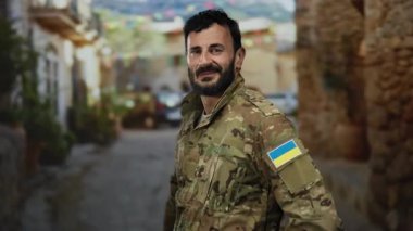 Ukrayna bayrağı gösteren askeri üniformalı sakallı bir adam açık bir sokakta duruyor..