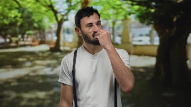 Sakallı İspanyol bir adam açık havada keyif ve haz sunan ağaçlarla çevrili yemyeşil bir parkta şef öpücüğü jesti yapıyor..