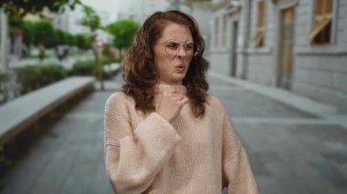 Şehir caddesinde gözlük ve süveter takan kadın bulutlu atmosferde nötr duygular sergiliyor..