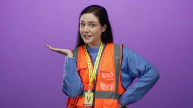 Kadın gönüllü turuncu yelek giymiş canlı mor arka plana karşı jestler yaparak rolünü sergiliyor.