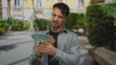 Genç İspanyol adam güneşli bir şehir caddesinde mutlu bir ifadeyle Brezilya 'nın gerçek banknotlarını sayıyor..
