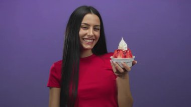 Elinde dondurmayla gülümseyen, mor arka planda kırmızı gömlekli bir kadın.