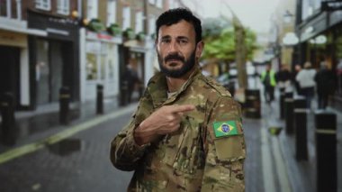 Sakallı, kamuflaj üniformalı bir asker Brezilya bayrak kuşağını işaret ediyor açık bir şehir caddesinde hareketli duruyor..